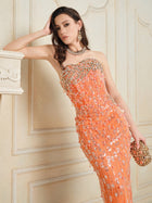 A woman poses indoors wearing the Social Queen Beaded Crystal Strapless Gown, styled with a matching clutch, elegant jewelry, and wavy side-swept hair.