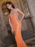 A woman stands in an ornate hallway wearing the Social Queen Beaded Crystal Strapless Gown, featuring a fitted silhouette with intricate beading and sequins. She holds a gold clutch and gazes to the side.