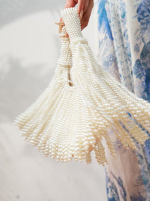 A hand holds the Social Queen Beaded Fan Tassel Handbag, featuring tassel accents, beside a blue and white patterned garment.