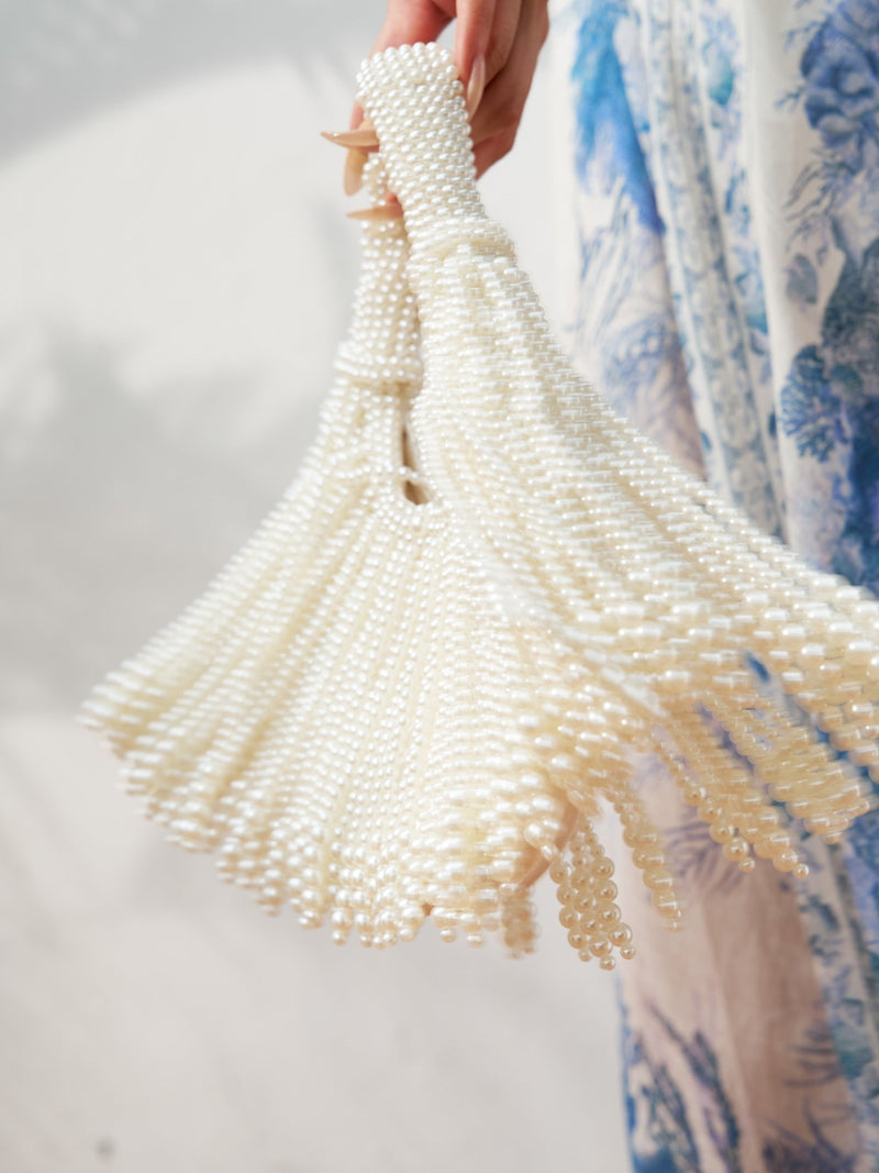 A hand holds the Social Queen Beaded Fan Tassel Handbag, featuring tassel accents, beside a blue and white patterned garment.