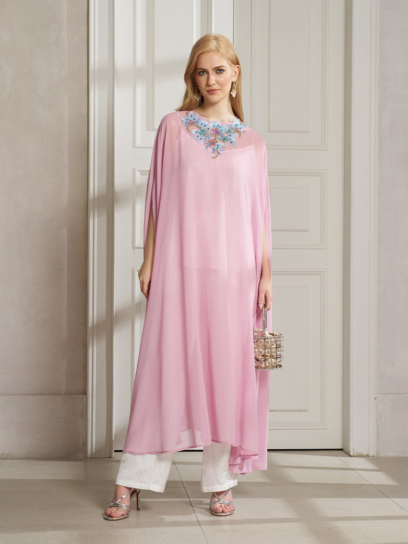 Indoors, a person wears the Social Queen Beaded Floral Chiffon Top with white pants, silver heels, and holds a small handbag.