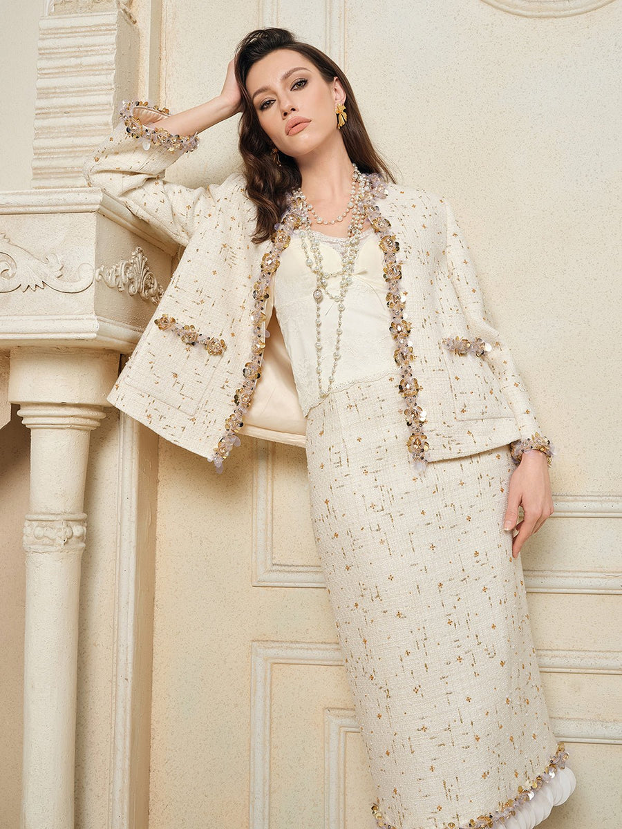 A woman stands indoors in the Social Queen Beaded Floral Embroidered Tweed Jacket, styled with a white blouse and long layered necklaces, leaning against a fireplace mantel.