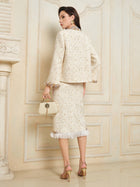 A woman in the Social Queen Beaded Floral Embroidered Tweed Jacket with a matching skirt and handbag stands facing a decorative wall, her back to the camera.