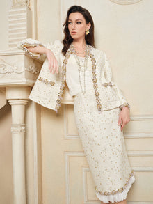 A woman wearing the Social Queen Beaded Floral Embroidered Tweed Skirt, an elegant cream-colored design with gold accents and 3D floral details, stands indoors leaning against a classical mantelpiece.