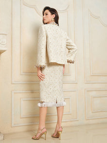 A woman stands facing a wall, wearing the Social Queen Beaded Floral Embroidered Tweed Skirt paired with gold high-heeled sandals.