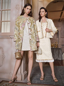 Indoors, one woman wears a printed coat and short dress, while the other shines in Social Queen's Beaded Floral Embroidered Tweed Skirt, paired with heeled sandals; both have styled hair.