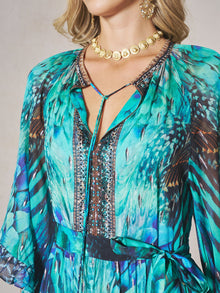 A woman in Social Queen's Beaded Floral Print Ruffled Dress, styled with a gold coin necklace and gold earrings. Only her upper torso and part of her face are visible.