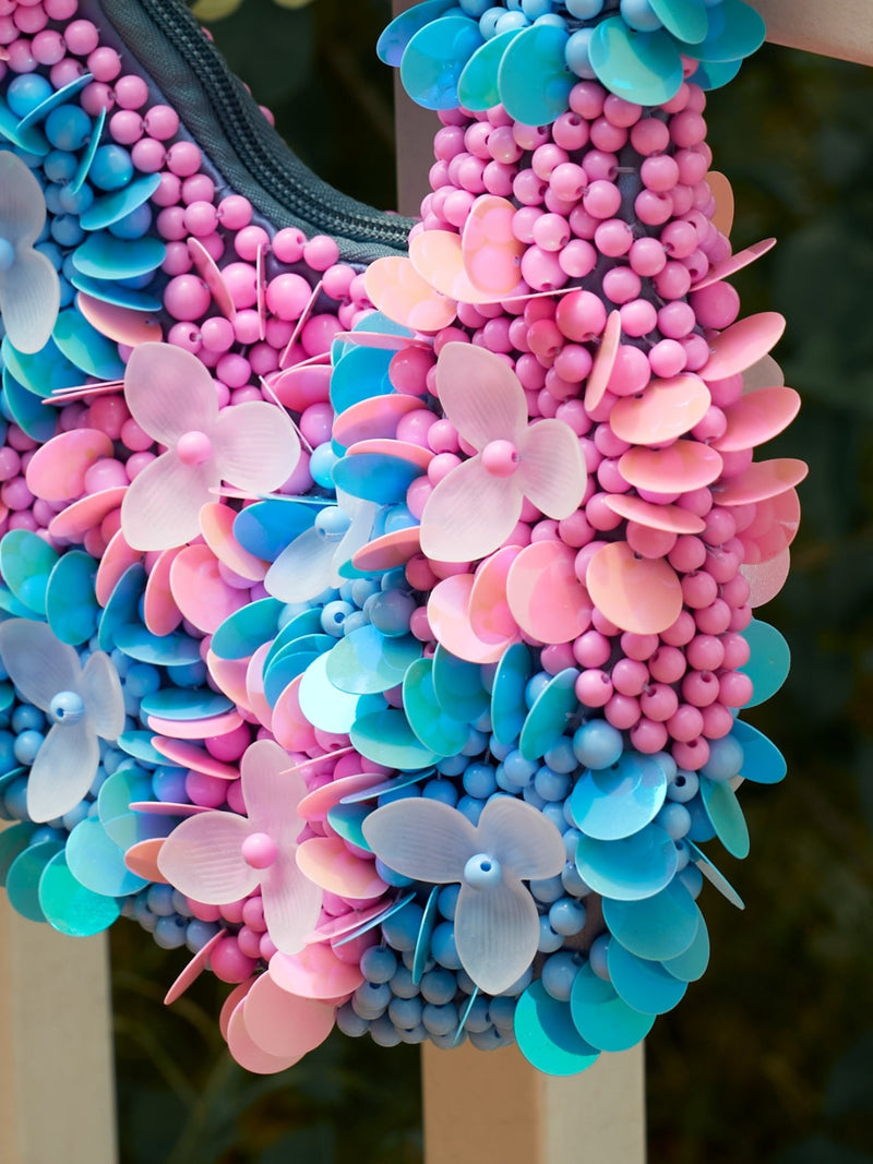A close-up of the Beaded Floral Top-Handle Bag by Social Queen, featuring pink, blue, and peach plastic flowers and beads with intricate, colorful dimensional floral detailing.