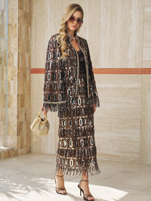 A woman wearing sunglasses, strappy heels, and a black top pairs the Social Queen Beaded Fringe Sequin Midi Skirt with a small woven handbag as she stands in a sunlit, tiled space.