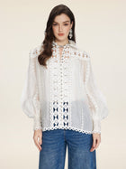 A woman in the Social Queen Beaded Geometric Lace Blouse with lantern sleeves and hand-crocheted details pairs it with blue jeans, standing against a plain beige background.