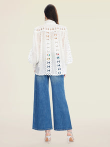 A woman stands facing away, wearing the Social Queen Beaded Geometric Lace Blouse with lantern sleeves, wide-leg blue jeans, and white heeled sandals.