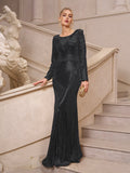 A woman in the Social Queen Beaded Gold-Accent Crystal Gown stands on a staircase holding a gold clutch, with classical statues behind her—an elegant evening gown or chic choice for a wedding guest.