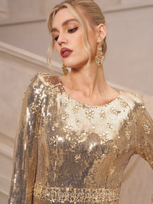 A woman in the Social Queen Beaded Gold-Accent Crystal Gown with matching earrings, ideal for a wedding guest, stands against a neutral-toned backdrop.