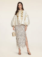 A woman wears the Social Queen Beaded Jacquard Lantern Sleeve Jacket with a silver fringed skirt, strappy heels, and a small gold handbag against a plain background.