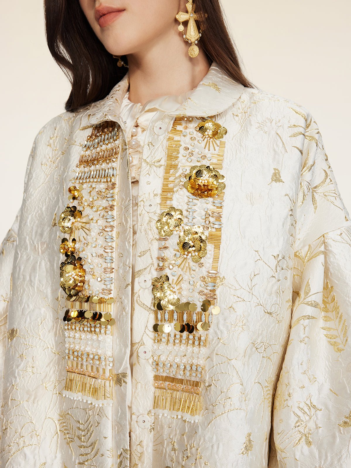 A woman wears the Social Queen Beaded Jacquard Lantern Sleeve Jacket, featuring hand-applied beads and gold accents, paired with gold drop earrings.