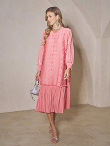 A woman in a Social Queen Beaded Jacquard Pleated Midi Dress stands indoors, holding a small silver handbag and wearing silver sandals with statement jewelry.
