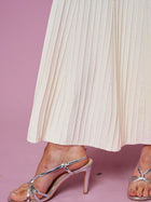 A person wearing the Social Queen Beaded Knit Pleated Dress stands on a pink surface, paired with silver high-heeled sandals.