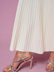 A person wearing the Social Queen Beaded Knit Pleated Dress stands on a pink surface, paired with silver high-heeled sandals.