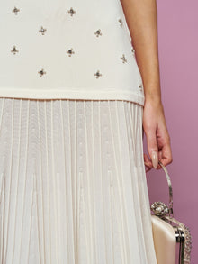 A person poses against a pink background wearing the Social Queen Beaded Knit Pleated Dress and holding a small, pale clutch purse.