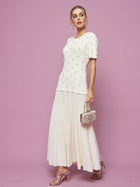 A woman poses against a pink background in the Social Queen Beaded Knit Pleated Dress, paired with silver heels and a decorative handbag.