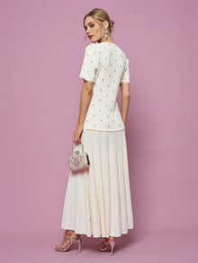 A woman in the Social Queen Beaded Knit Pleated Dress holds a small embellished handbag, posing against a pink background.