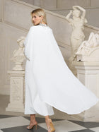 A woman in the Social Queen Beaded Mock-Neck Cape Dress and high heels stands on a checkered floor near classical statues and a staircase.