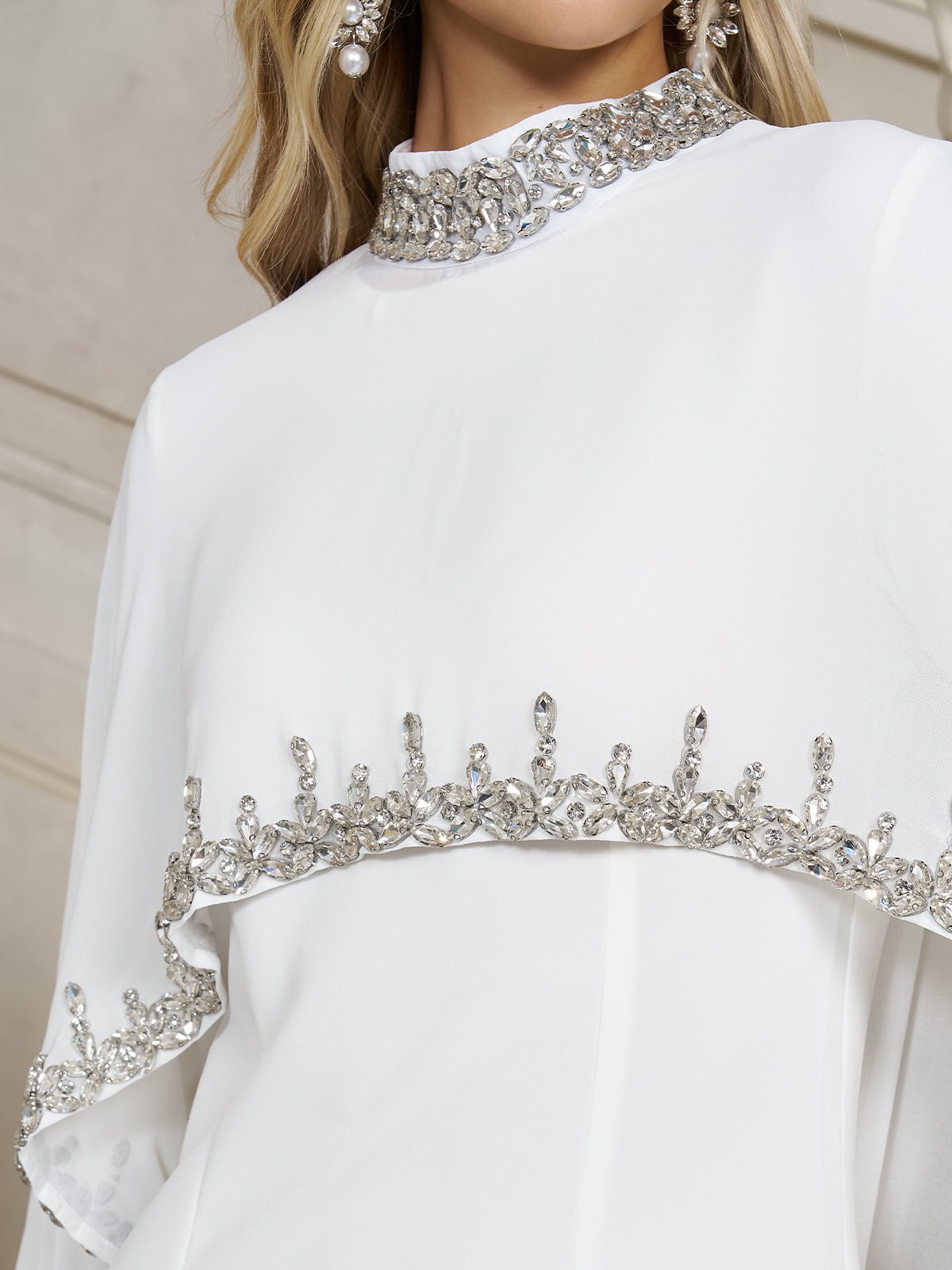 Close-up of the Beaded Mock-Neck Cape Dress by Social Queen in white chiffon, detailed with silver embellishments on the neckline, chest, and sleeves—a sophisticated option for wedding guests.