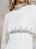Close-up of the Beaded Mock-Neck Cape Dress by Social Queen in white chiffon, detailed with silver embellishments on the neckline, chest, and sleeves—a sophisticated option for wedding guests.