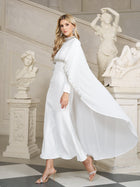 Wearing the Social Queen Beaded Mock-Neck Cape Dress, a woman with elegant trim strolls past white classical statues in a stunning marble interior.