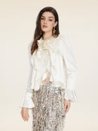 A woman wears the Social Queen Beaded Ruffle Satin Blouse, featuring hand-stitched ruffles and puff sleeves, paired with a silver sequin fringed skirt, posing against a plain light background.