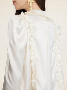 A woman models the Social Queen Beaded Ruffle Satin Blouse in white with puff sleeves and hand-stitched ruffles, paired with gold statement earrings, shown from side and back.
