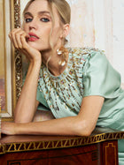 A woman in the Social Queen Beaded Satin Evening Gown rests her chin on her hand, leaning on a wooden surface and gazing at the camera.