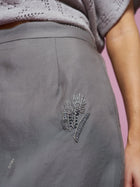 Close-up of a person wearing the Social Queen Beaded Silk Organza Midi Skirt, featuring beaded floral embroidery near the hip and a midi silhouette, paired with a textured gray top; light pink background.