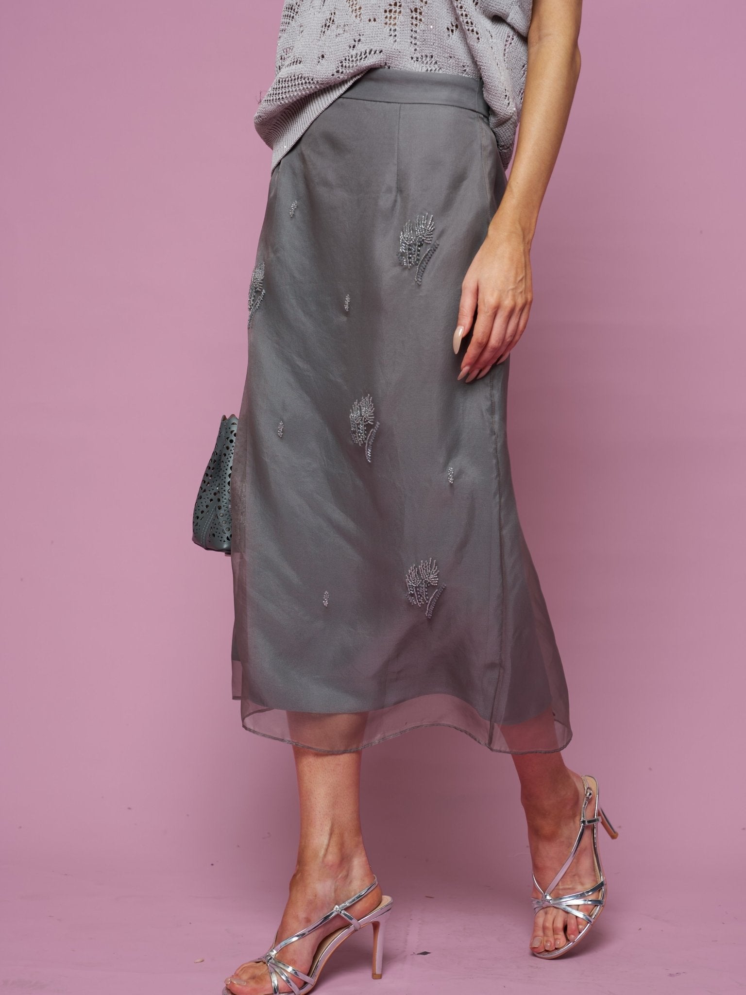 A person in a Social Queen Beaded Silk Organza Midi Skirt, sleeveless knit top, and strappy heeled sandals stands against a pink background.