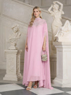 A woman in the Social Queen Beaded Tulle Caftan Cape Dress stands indoors by white classical sculptures, holding a small embellished handbag and wearing heeled sandals.