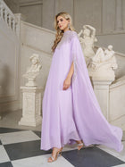 A woman in a Beaded Tulle Caftan Cape Dress by Social Queen and heels walks indoors past classical sculptures and marble stairs.