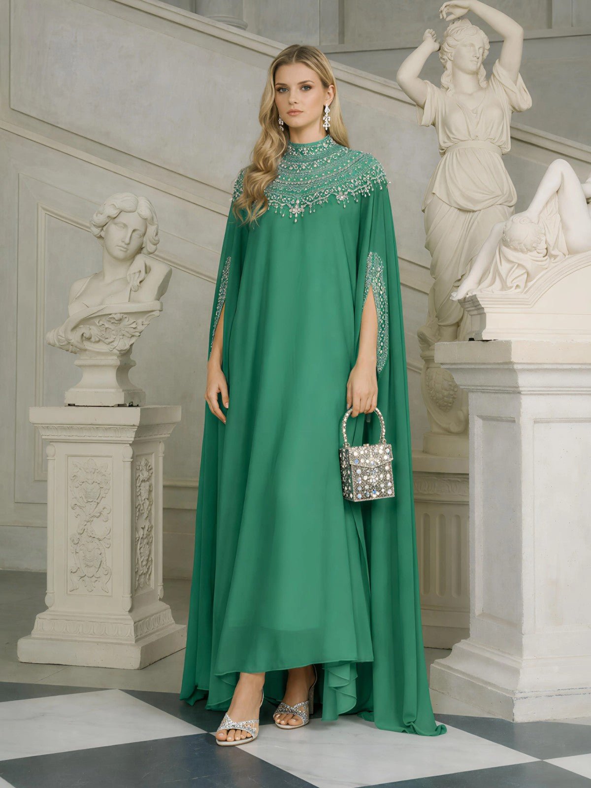 A woman in a Social Queen Beaded Tulle Caftan Cape Dress holds a rhinestone handbag, surrounded by white classical statues and ornate architecture.
