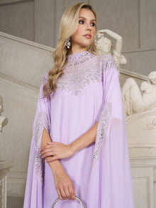 A woman in the Social Queen Beaded Tulle Caftan Cape Dress stands before classical statues and a marble staircase, gazing to the side.