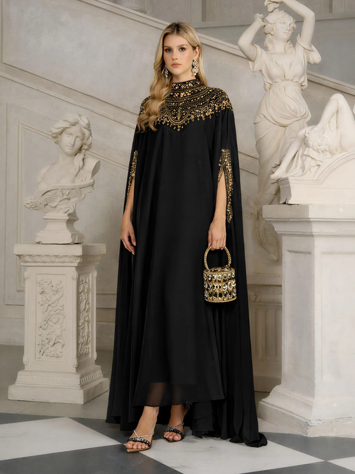 A woman stands in an ornate room wearing the Social Queen Beaded Tulle Caftan Cape Dress, holding a small decorated handbag and surrounded by classical statues.