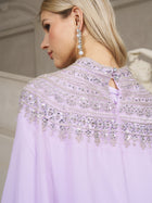 A woman with long blonde hair wears the Social Queen Beaded Tulle Caftan Cape Dress adorned with lavender beads, silver sequins, and a long pearl earring.