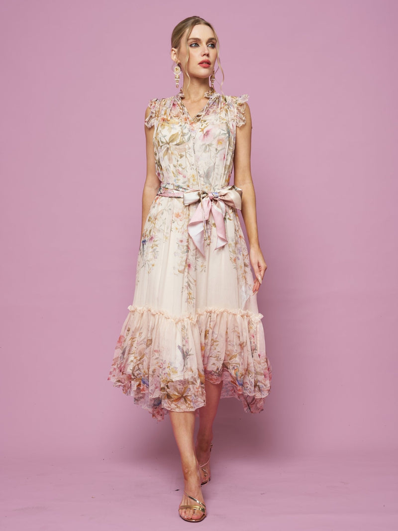 A woman wears the Social Queen Bird Floral Print Silk Dress featuring a sleeveless A-line silhouette, pink ribbon belt, and ruffled hem, standing against a solid pink background.
