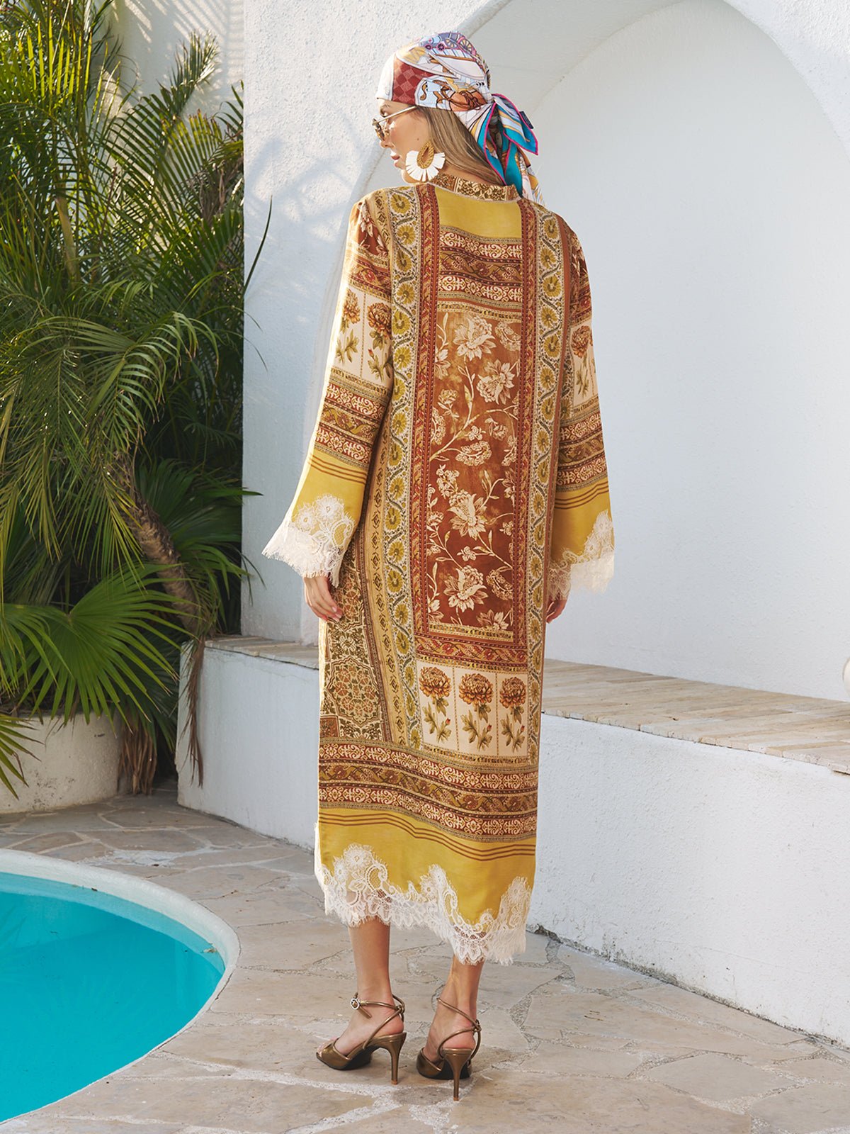 A person stands by a pool in the Social Queen Boho Lace Floral Print Dress, featuring handcrafted lace panels, styled with strappy sandals, statement earrings, and a vibrant headscarf.