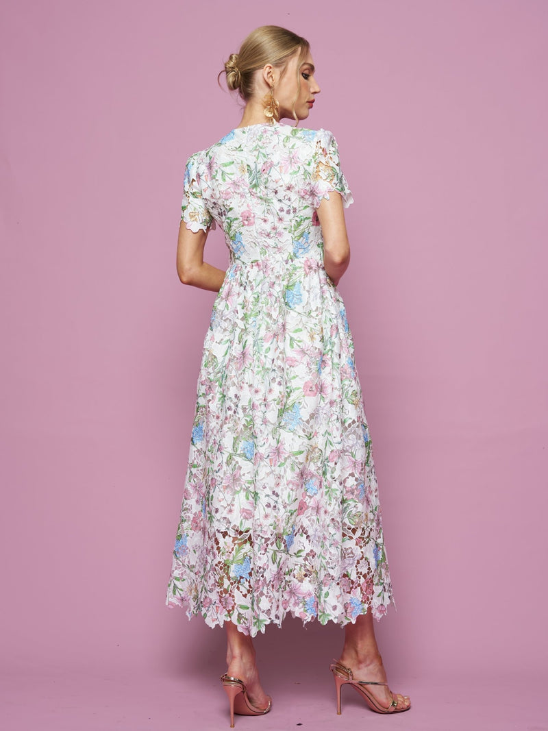A woman faces away against a pink background, wearing the Social Queen Botanical Embroidered Cutout Dress with an A-line silhouette and short sleeves, paired with pink high-heeled sandals.