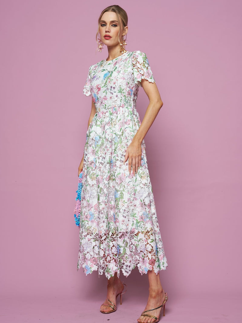 A woman poses against a pink background in the Social Queen Botanical Embroidered Cutout Dress, featuring an A-line silhouette, short sleeves, and heeled sandals.