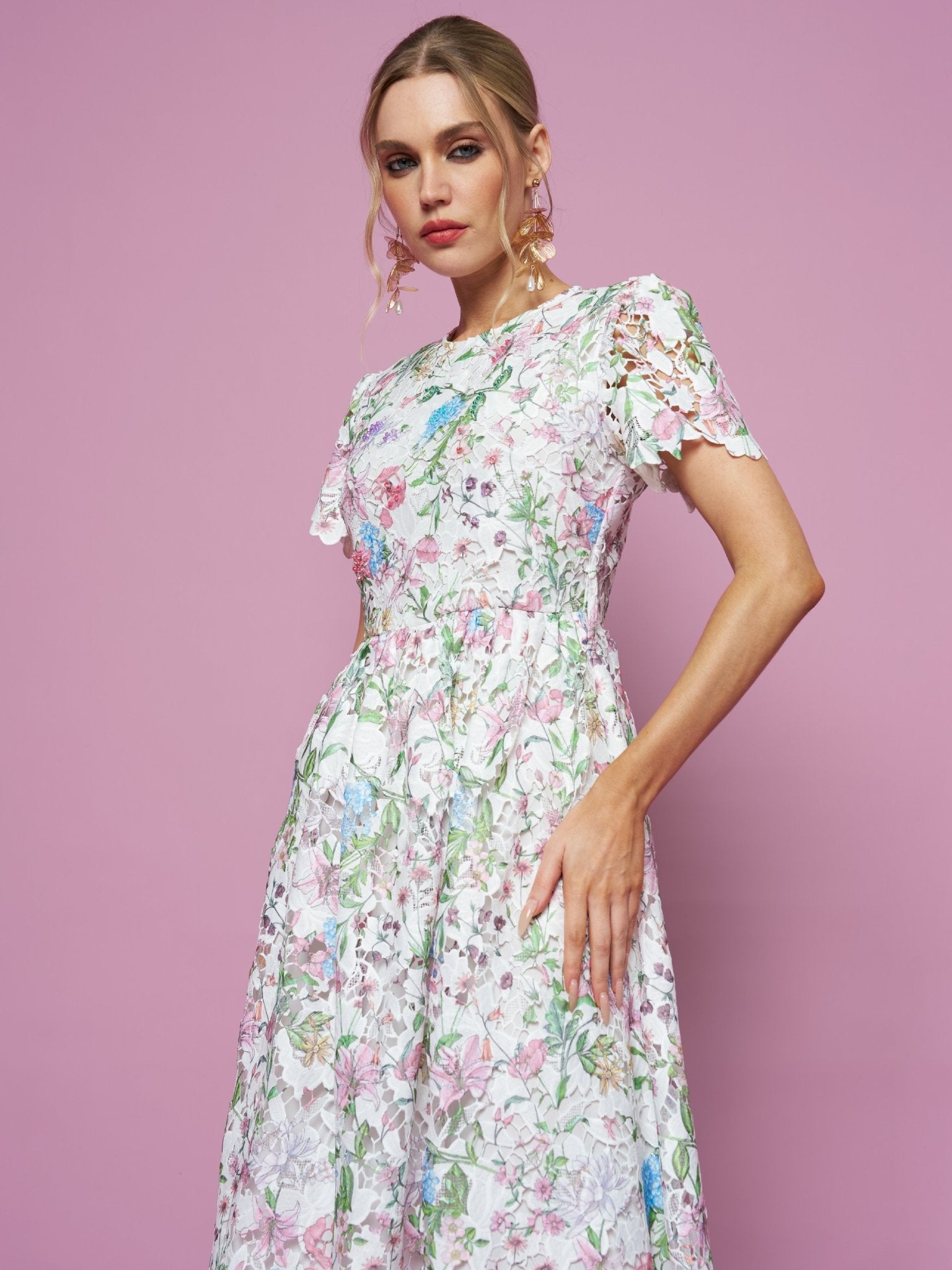A woman models the Social Queen Botanical Embroidered Cutout Dress, featuring short sleeves and an A-line silhouette, against a solid pink background.