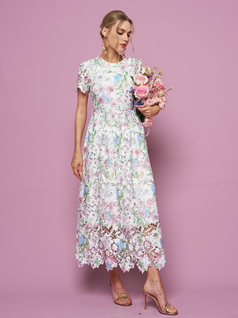 Woman wearing the Social Queen Botanical Embroidered Cutout Dress, featuring an A-line silhouette, holds a bouquet of pink flowers against a pink backdrop, paired with gold high-heeled sandals.