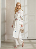 A woman stands indoors wearing Social Queen's Botanical Embroidered Linen Top and pants, paired with silver heels and a small handbag, showcasing elegant ethnic-inspired embroidery.