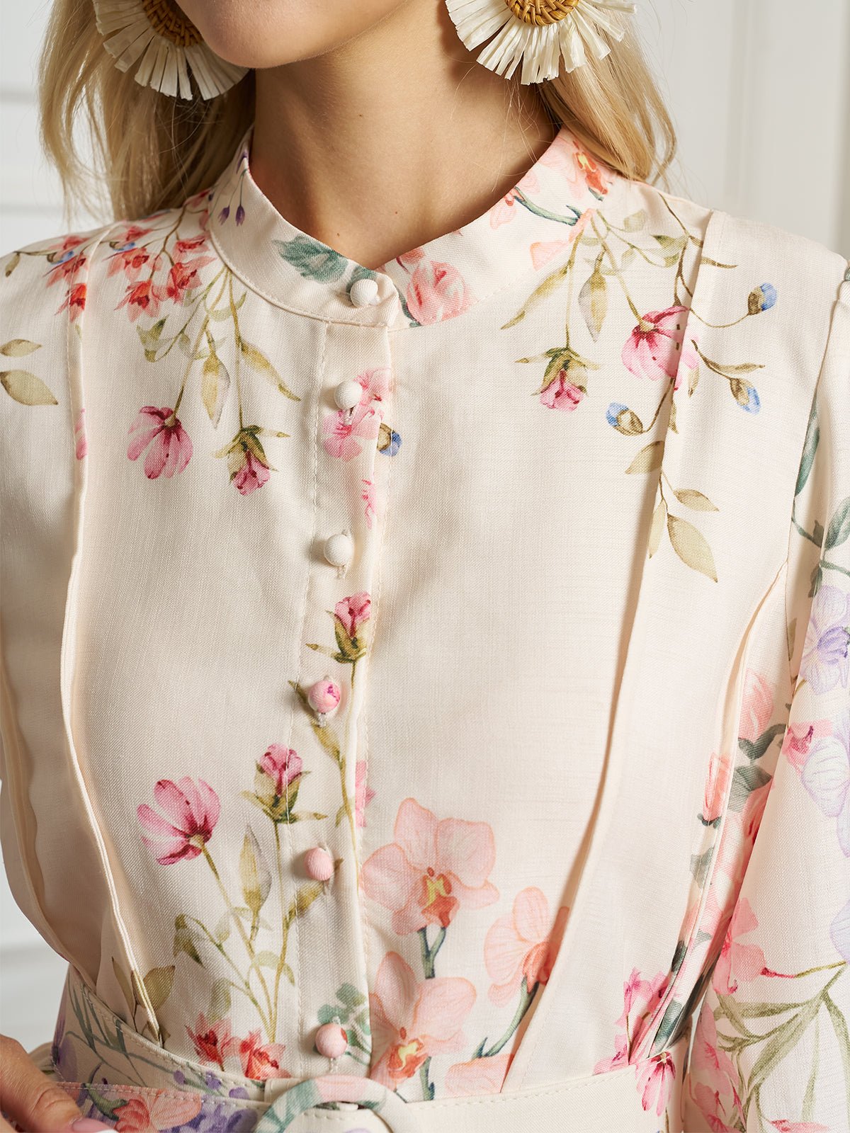 Close-up of a woman in Social Queen’s Botanical Print Cotton-Linen Dress, featuring a light floral pattern, fabric-covered buttons, and pleats. She pairs it with large floral earrings.
