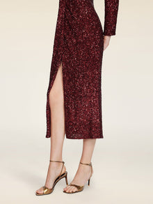 A model wears the Social Queen Burgundy Sequin V-Neck Slit Dress, featuring a ruched waist and thigh-high slit, paired with gold high-heeled sandals, shown from shoulder to feet against a plain background.