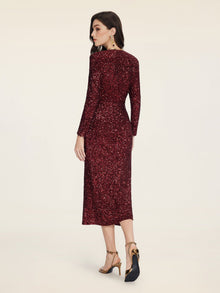 A woman in the Social Queen Burgundy Sequin V-Neck Slit Dress with gold heels stands against a plain light background, facing away from the camera.